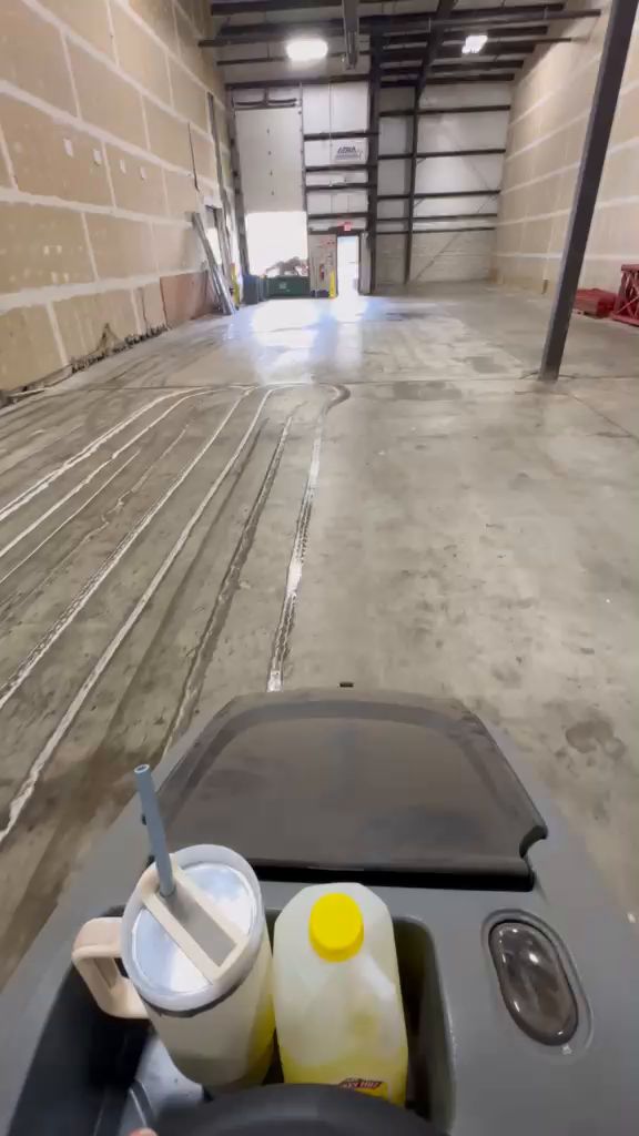 Ride-on floor scrubber cleaning a warehouse floor before turnover